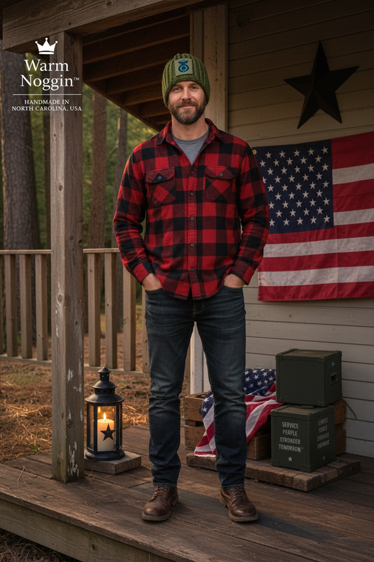 A man stands on a rustic wooden porch wearing a red and black buffalo plaid flannel shirt, dark blue jeans, and a green beanie. A warm white 'Warm Noggin' logo is visible in the top left corner, and an American flag hangs on the wall behind him.