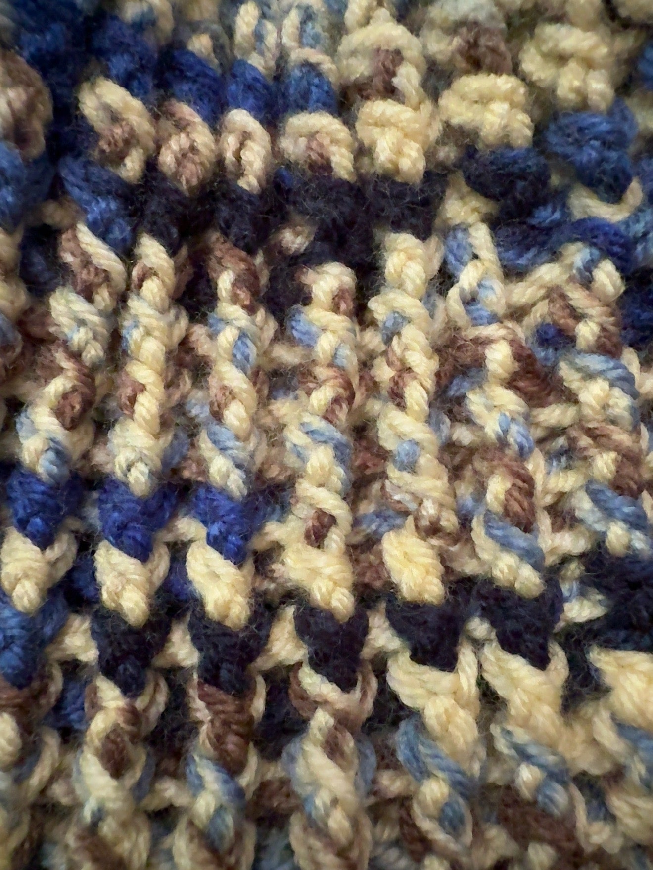 Close-up of a chunky crochet fabric with a textured pattern in cream, navy blue, and brown yarn.