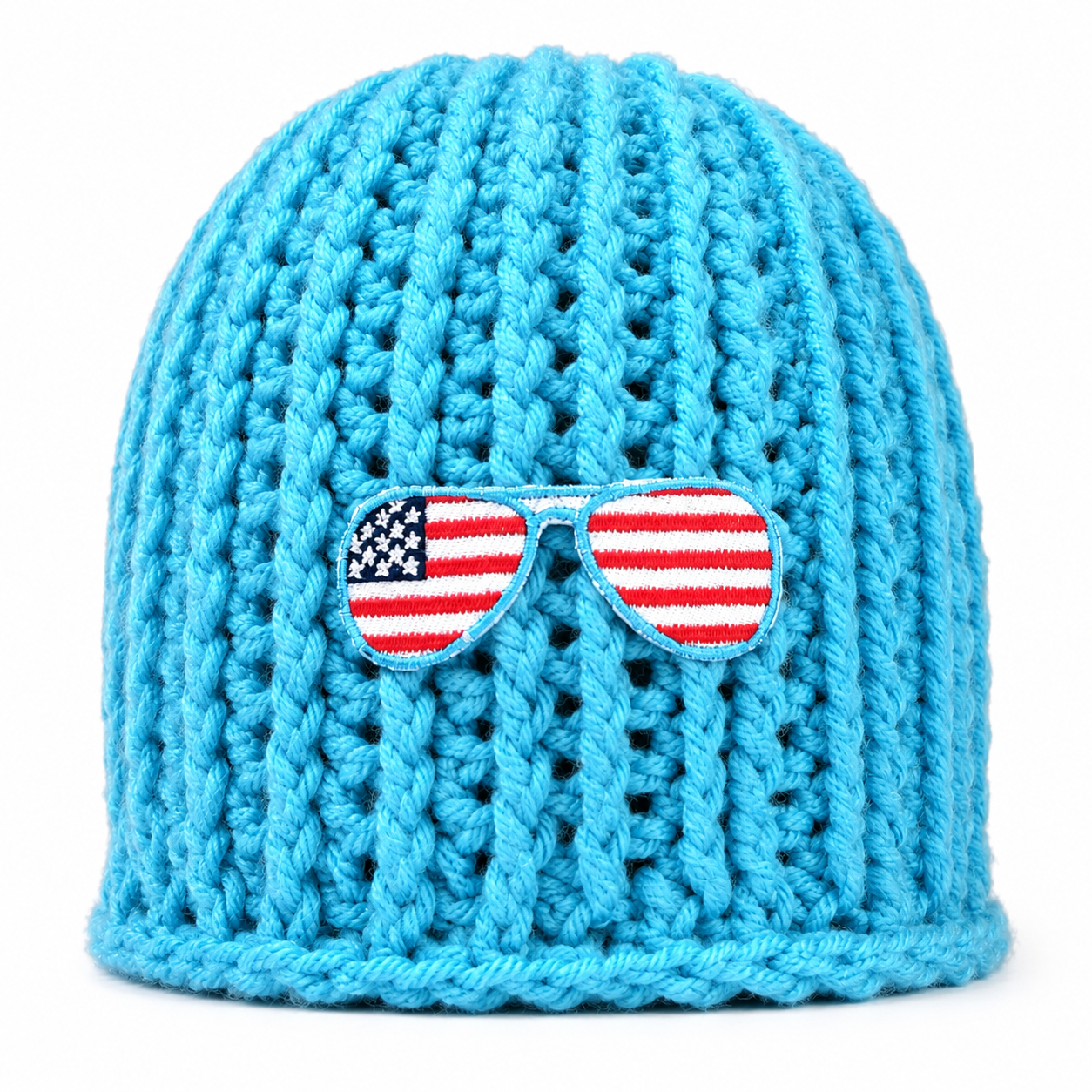 A bright blue chunky crochet beanie hat featuring a decorative embroidered patch of sunglasses with an American flag design on the front.