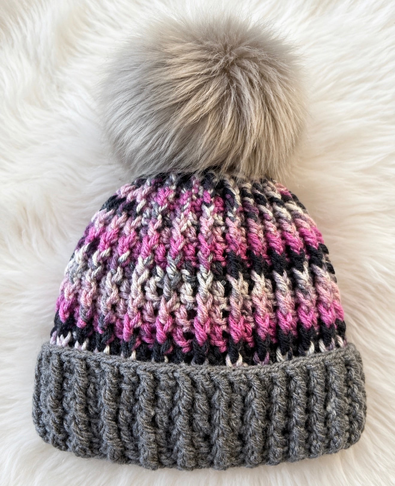 Ash and Orchid™ handmade crochet beanie featuring orchid pink, charcoal, and gray variegated yarn, oversized gray ribbed brim, and oversized faux fur pom showing close up