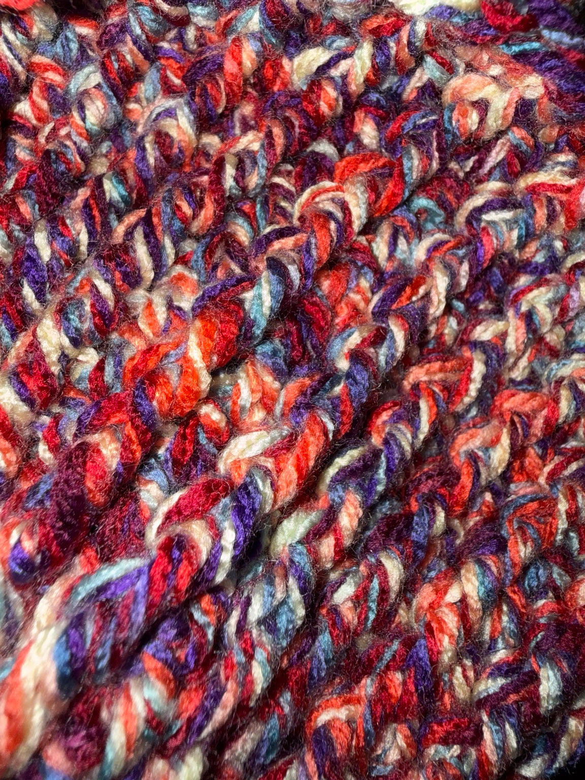 Close-up of variegated yarn with a chunky crochet texture, featuring blended shades of red, purple, blue, orange, and cream.