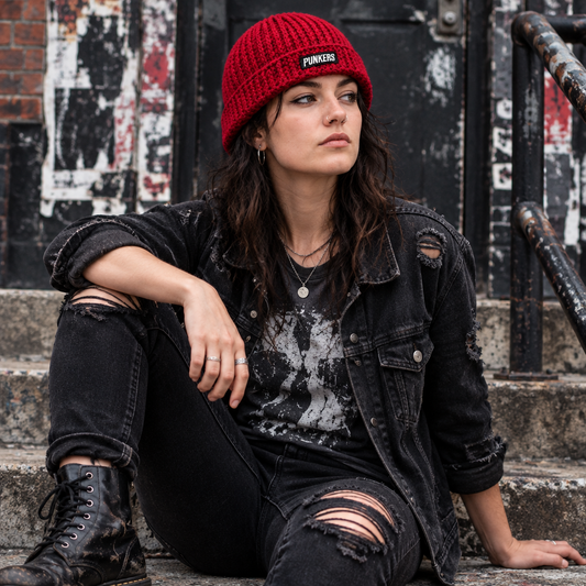 Rock Anthem™ No. 12 handmade crimson punk rock crochet beanie with brim and hand-stitched black PUNKERS patch, shown worn outside a live-music venue.