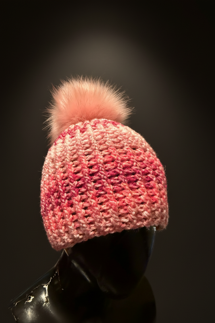 Pink crochet beanie with a fluffy pom-pom on a black background