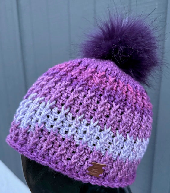Violet Frost Classic Ribbed Beanie in hues of purple with a dark purple pom against a grey wood panel wall
